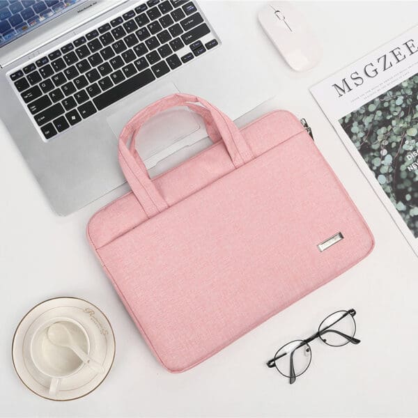 Chic pink laptop bag with silver laptop, mouse, coffee cup, and glasses for a stylish workspace.