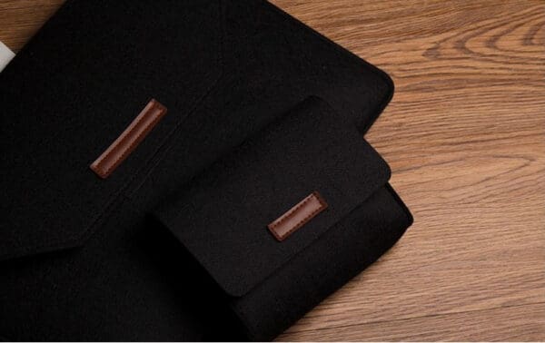 Elegant black felt laptop sleeve and pouch set with leather accents on a wooden surface.