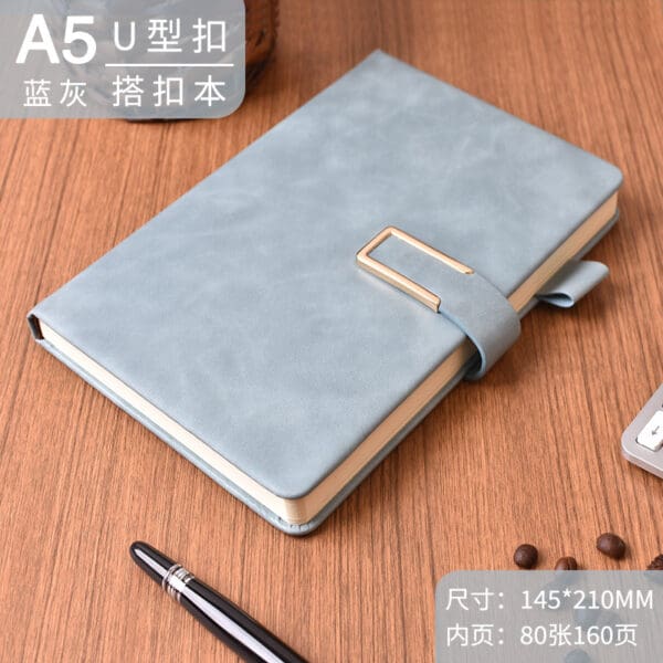 Stylish light blue A5 notebook with gold clasp and luxury pen on wooden surface.